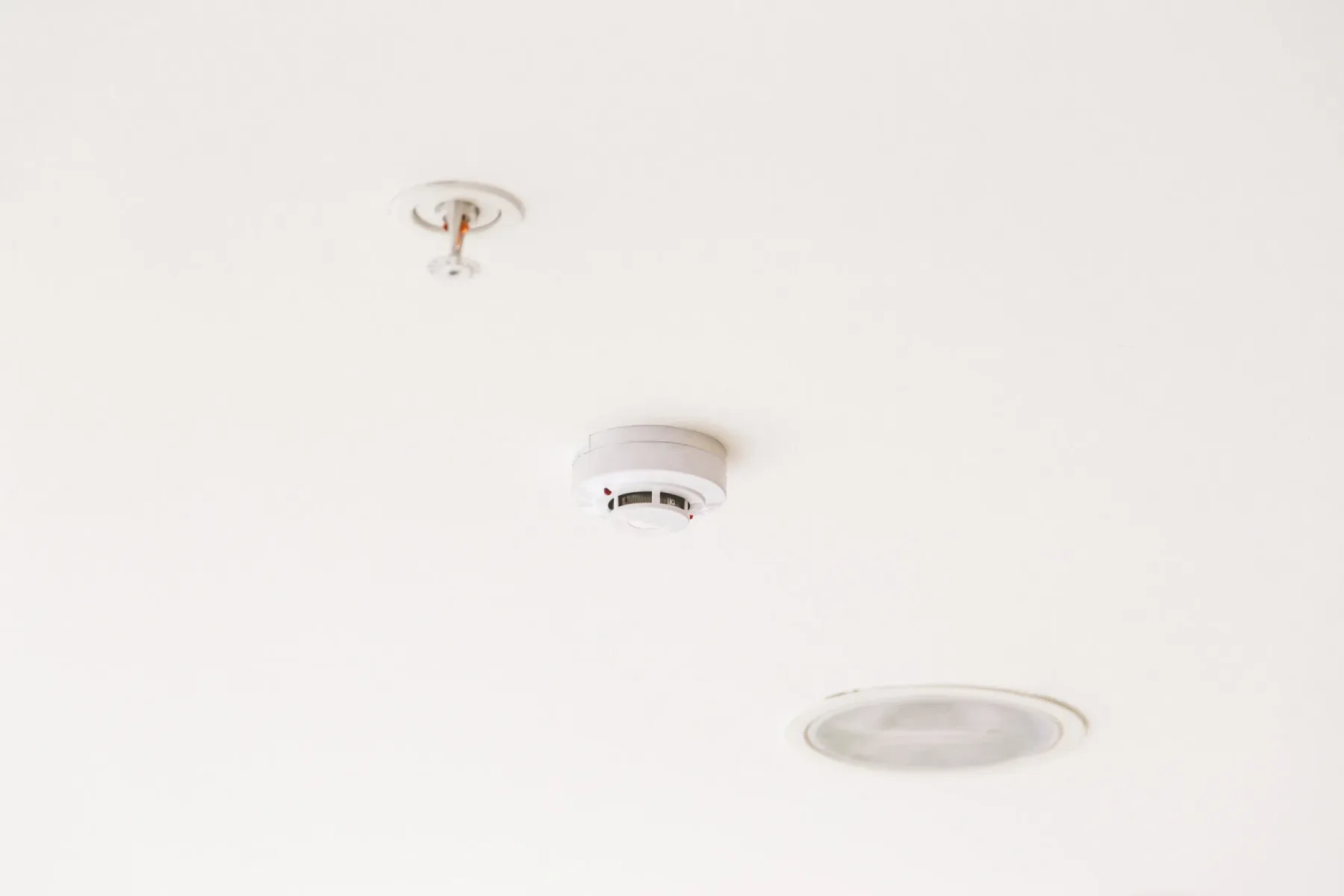 Smoke detector and sprinkler mounted on a white ceiling.