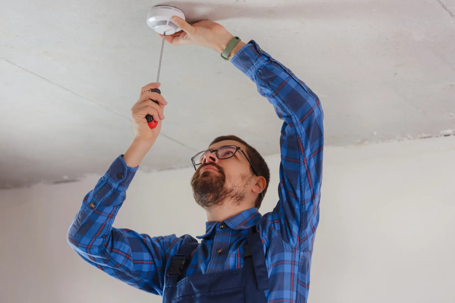 Technician installing a ceiling-mounted smoke detector.
